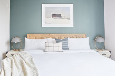 Coastal, cape cod bedroom with wood headboard, matching nightstands, lamps, blanket, pillows.